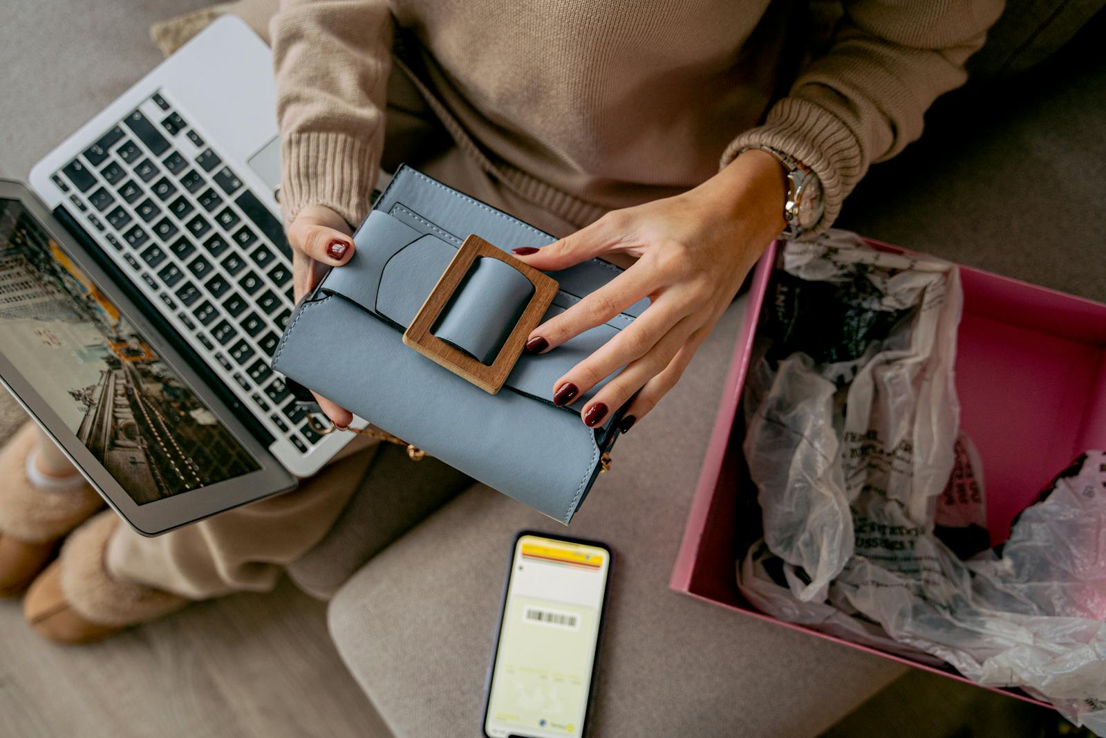 Woman unboxing a handbag using a laptop for online shopping at home.